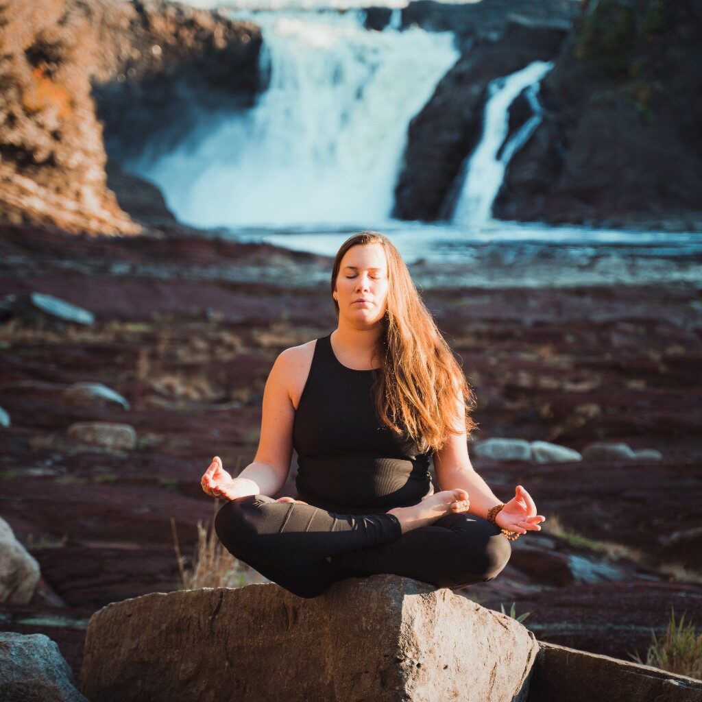 Eva Marquis Yoga assise devant les chutes de la chaudière dans la posture méditative du tailleur
